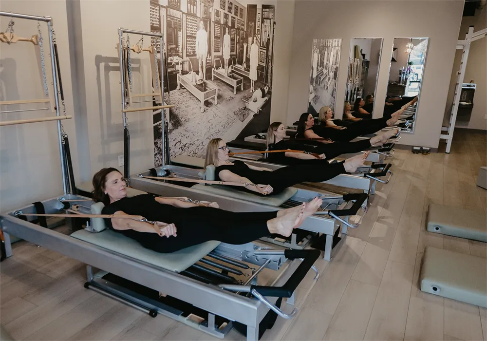 A group of women performing the Hundred exercise on the Reformer during a small group Pilates class in Louisville KY